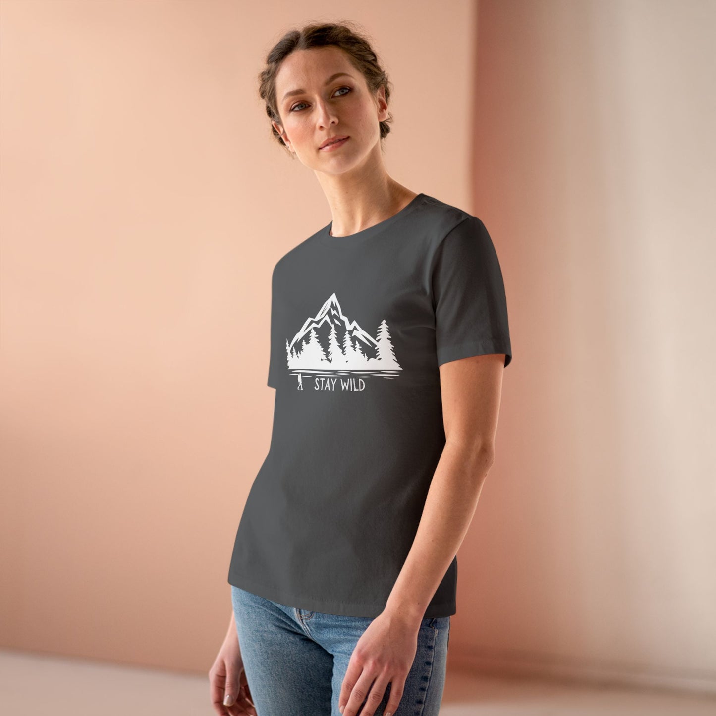 Woman wearing a dark gray t-shirt with a mountain graphic and 'Stay Wild' text on a beige background